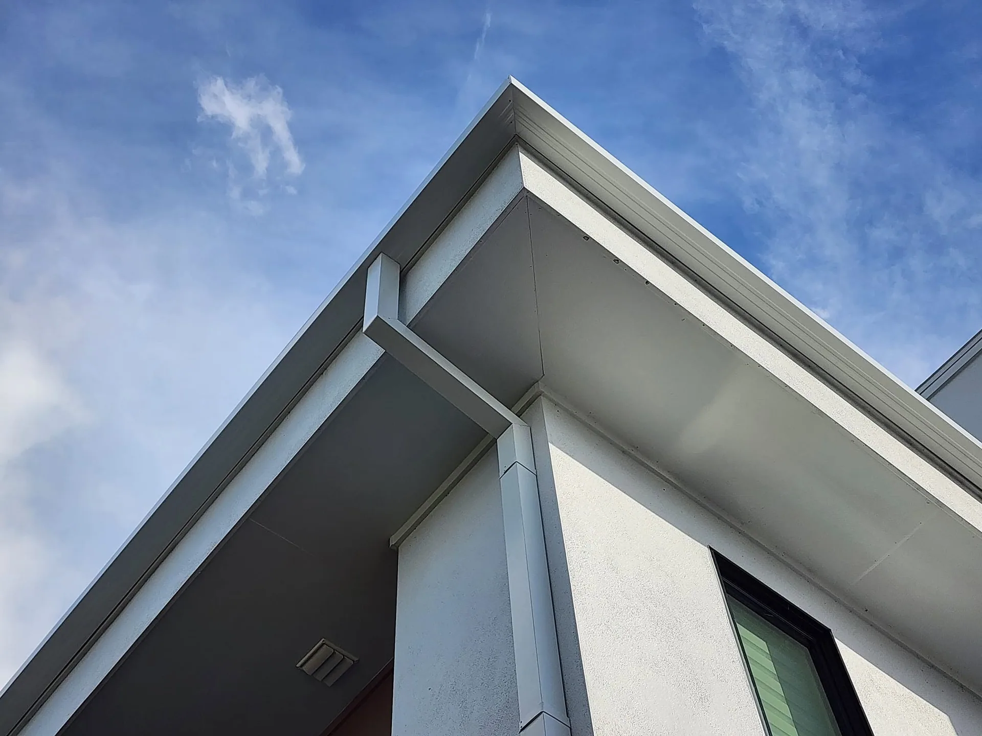 Low angle white square downspout corner smooth soffit modern flat roof, Sanford